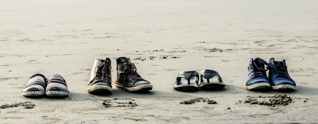 two pair of shoes and flip-flops on seashore near people at daytime